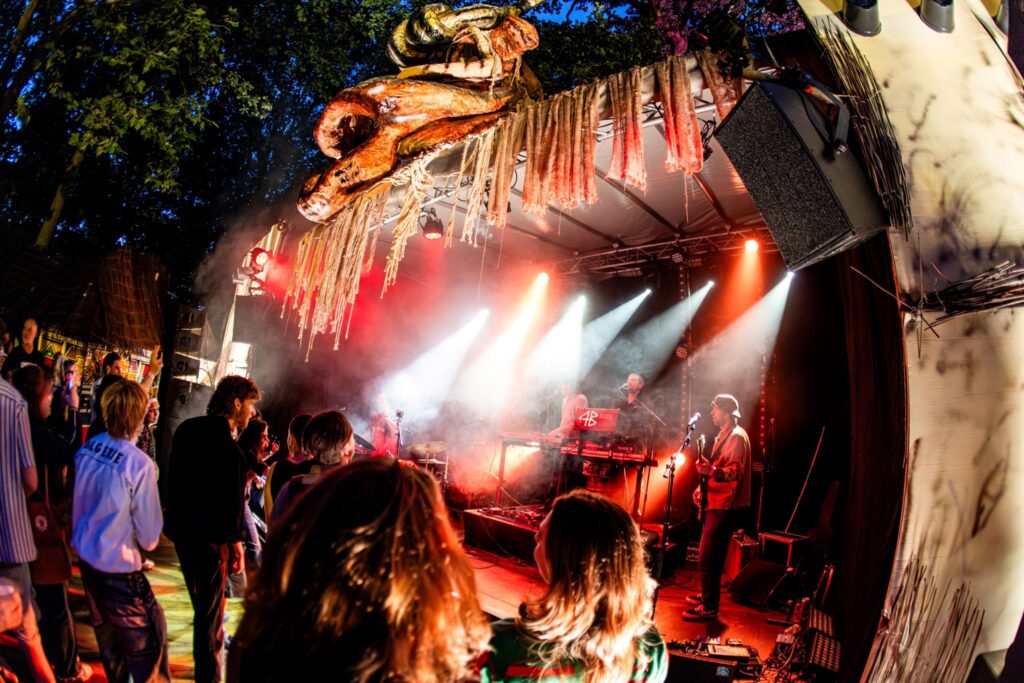 Festivalpubliek bij het hoofdpodium van Sungrooves Festival in Ravenstein, met kleurrijke verlichting en geluidsinstallatie geleverd door MAG Event Rental.