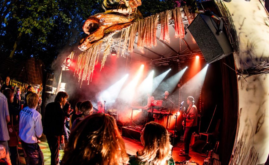 Festivalpubliek bij het hoofdpodium van Sungrooves Festival in Ravenstein, met kleurrijke verlichting en geluidsinstallatie geleverd door MAG Event Rental.